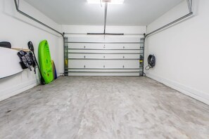Un garage propre et vide, avec un sol en béton, un kayak vert et une planche de paddle appuyée contre le mur.