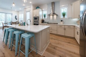 Una cocina moderna con una isla central, taburetes de bar, electrodomésticos de acero inoxidable y armarios de colores claros.