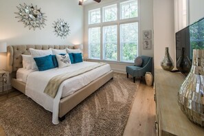 Un dormitorio con una cama grande, una ventana con persianas, un televisor y decoración en la pared.