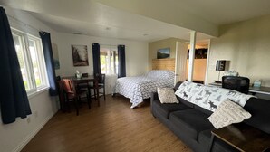 Ett rum med en säng, en soffa, ett matbord med stolar och ett fönster med gardiner.