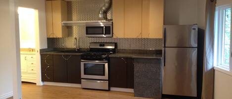 A modern kitchen with stainless steel appliances, dark wooden cabinets, and a tiled backsplash.