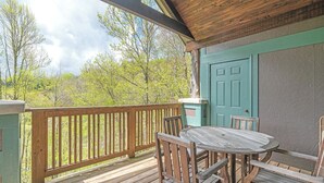 A wooden deck with a table and chairs, a green door, and a view of trees.