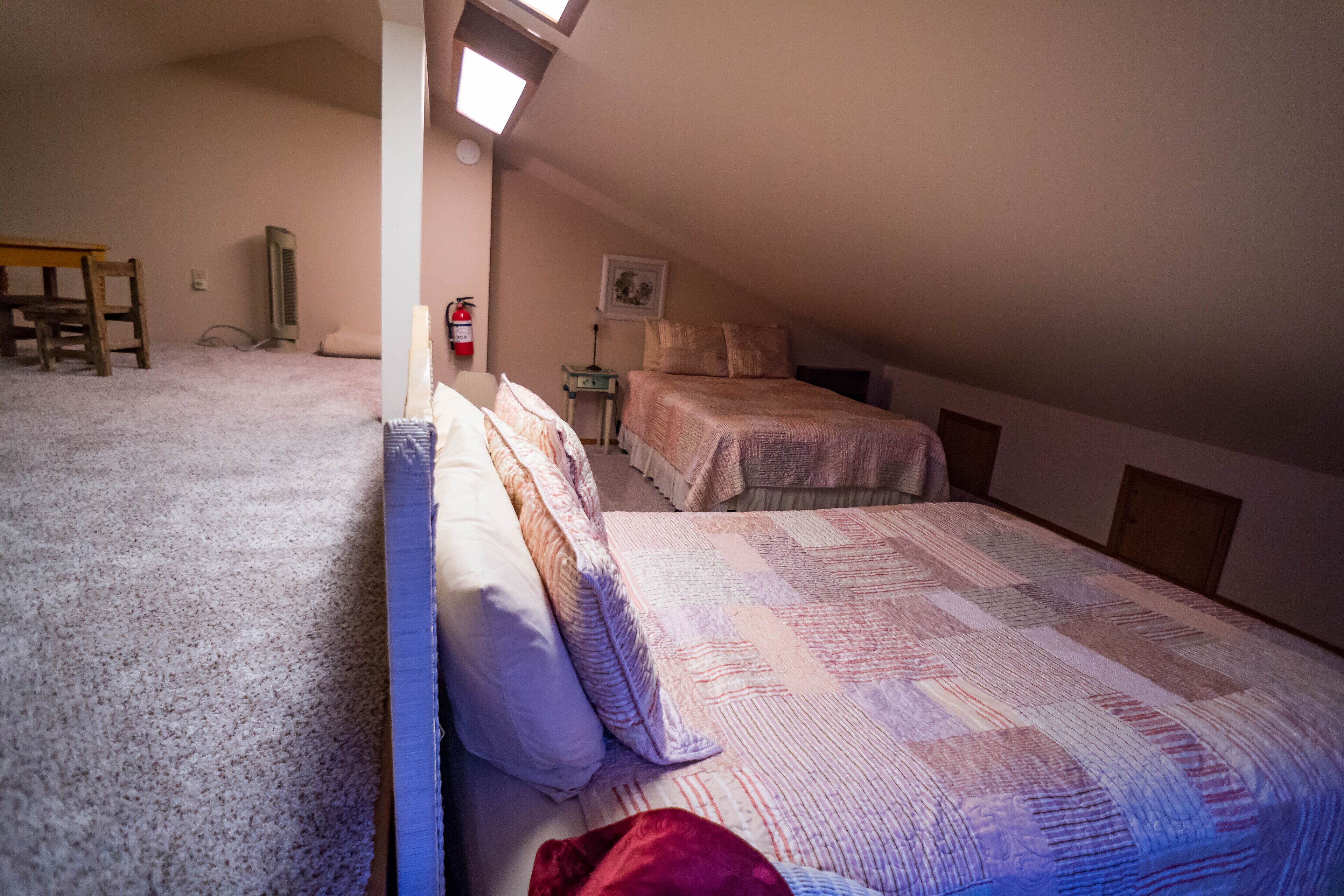 Un dormitorio con dos camas, una silla de madera, una mesita y un extintor.