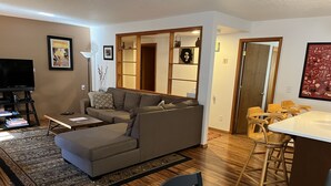 Una sala de estar con un sofá modular, una mesa de centro, un televisor y un comedor con sillas de madera y una mesa.