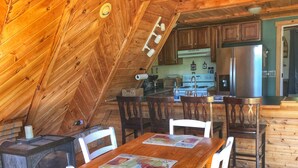 A cozy wooden cabin with a dining area featuring a wooden table and chairs, a fireplace, and a kitchen with wooden cabinets and appliances. - Secluded LAKEFRONT Chalet: 2.8acres, Dock, Kayaks and Canoe, Pet Friendly, Wifi (Butler)