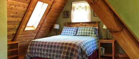 Een gezellig slaapkamer op zolder met een schuine plafond, een bed met geruit beddengoed, een klein nachtkastje en een nachttafel.