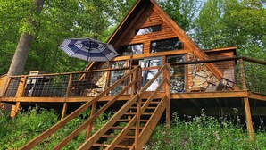 A cabin with a wooden exterior, a staircase leading to a deck, and a large umbrella. - Secluded LAKEFRONT Chalet: 2.8acres, Dock, Kayaks and Canoe, Pet Friendly, Wifi (Butler)