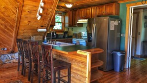 A rustic kitchen with wooden cabinets, a stainless steel refrigerator, and a bar area with stools. - Secluded LAKEFRONT Chalet: 2.8acres, Dock, Kayaks and Canoe, Pet Friendly, Wifi (Butler)