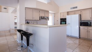 A modern kitchen with light-colored cabinets, a central island with bar stools, a refrigerator, microwave, and a stove. - PRIVATE CONTEMPORARY HOME WITH BREATHTAKING MOUNTAIN VIEWS (Tucson)