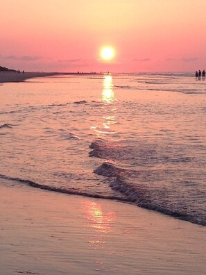 A sunset over a beach with waves reflecting the sun's light.
