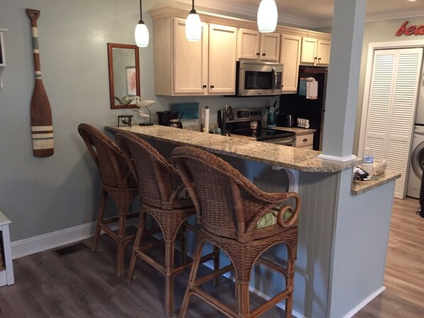 A kitchen with a bar area, wooden chairs, a microwave, and a sink.