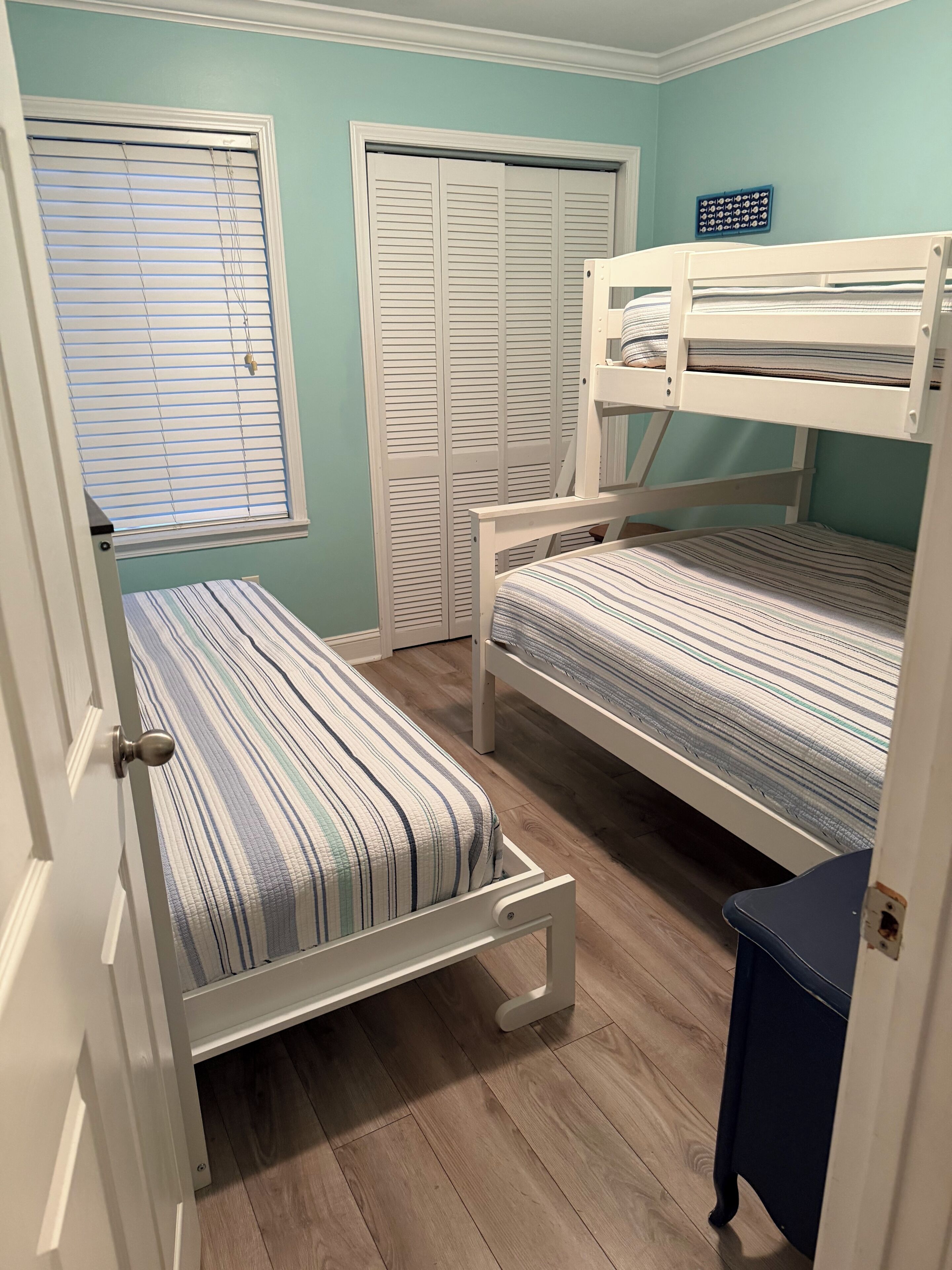 Quarto com beliches, porta com puxador, janela com persianas e um objeto fixado na parede.