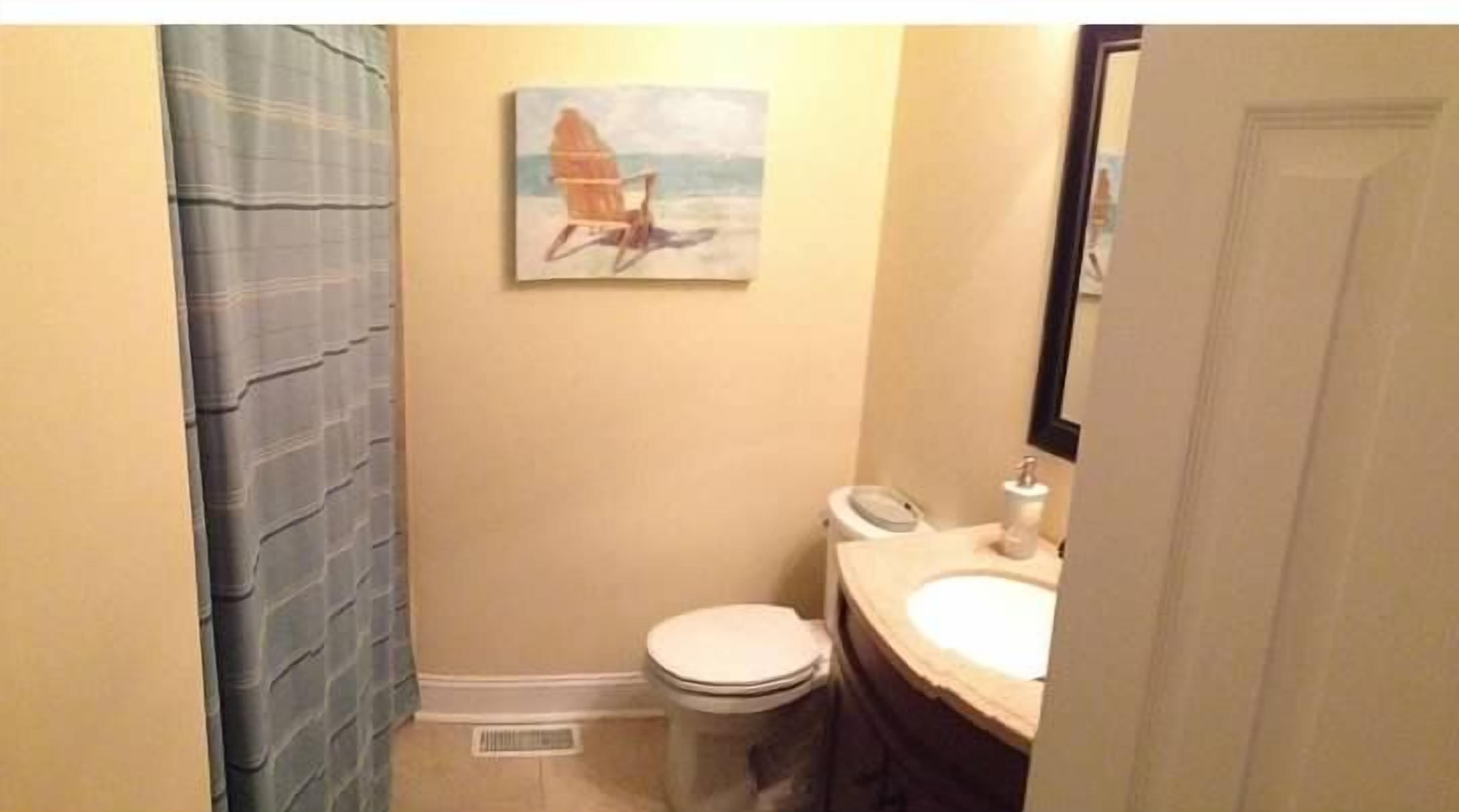 A small bathroom with a toilet, sink, and a painting of a sailboat on the wall.