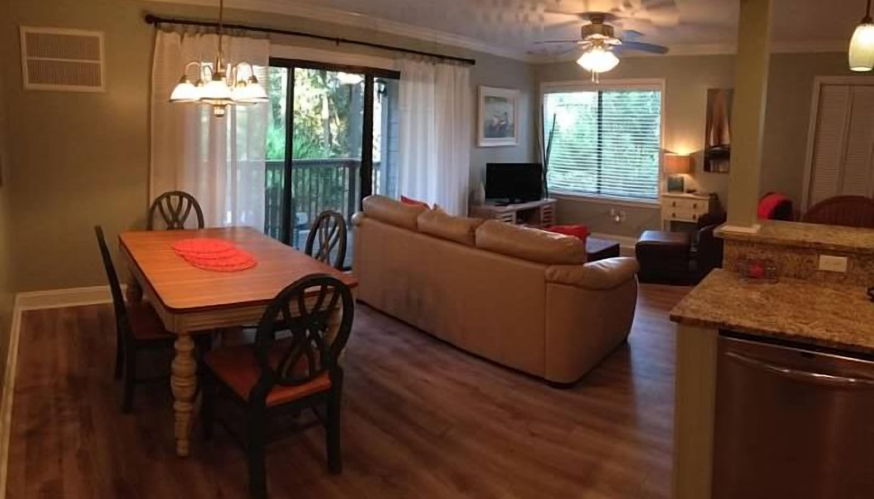 Un comedor con mesa y sillas de madera, un sofá color beige y una zona de cocina con encimera y electrodomésticos.