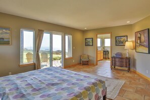 Un dormitorio con cama, una silla, un tocador y vistas al exterior.