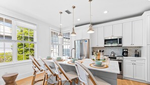 Una cocina moderna con gabinetes blancos, electrodomésticos de acero inoxidable y una isla grande con taburetes de bar.