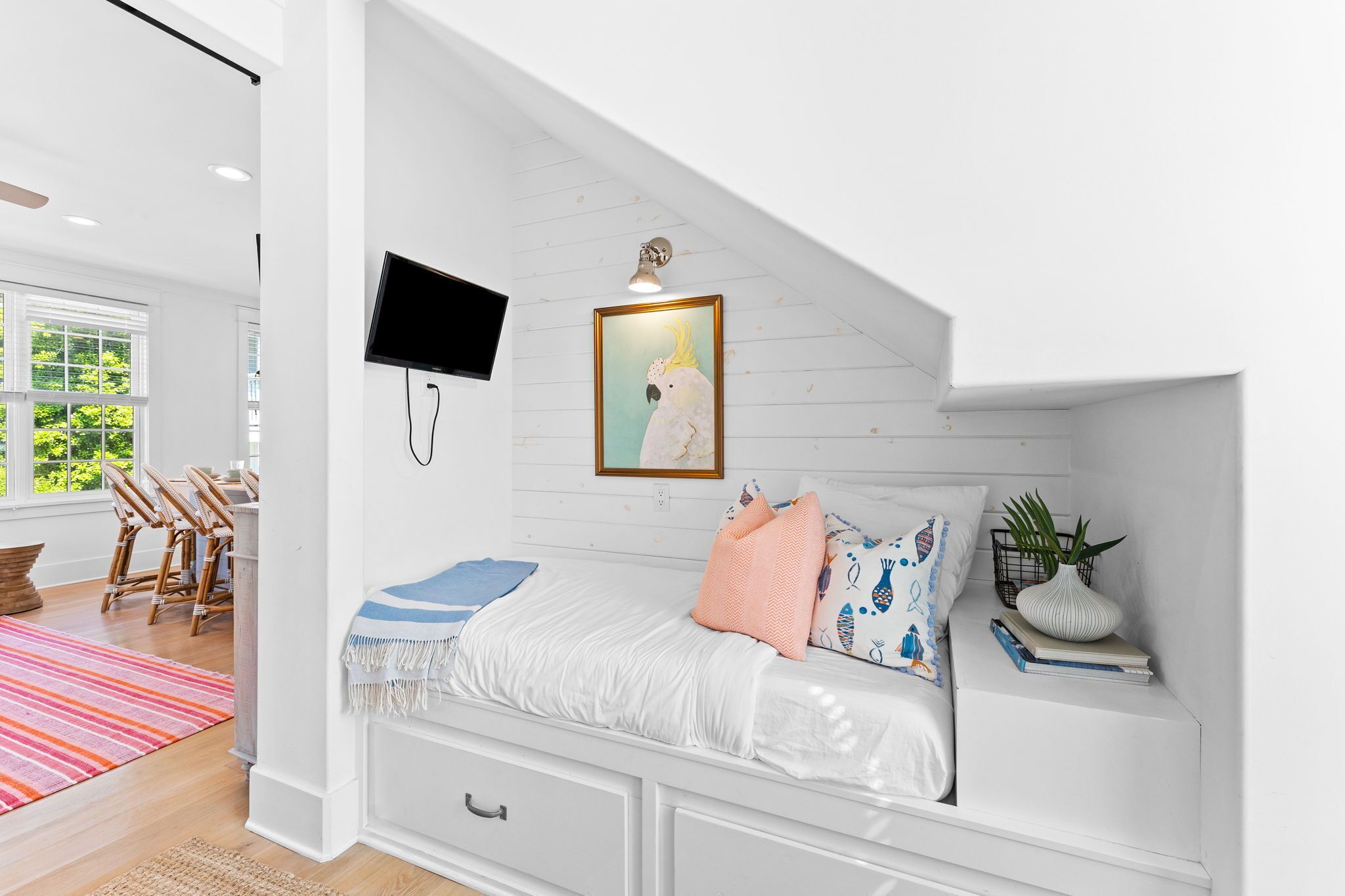 Une chambre à coucher avec un lit blanc, un tableau représentant un oiseau et un téléviseur fixé au mur.