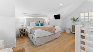 Un dormitorio con una cama grande, un televisor montado en la pared, una ventana con persianas y una planta.