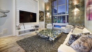 A modern living room with a large flat-screen TV, white sofas, a glass coffee table, and a large window with a city view. - Stunning Remodel 4 BR/3 BA Downtown ,Gaslamp, Petco, Convention Center (San Diego)
