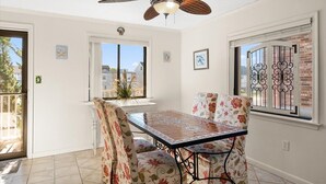 Un comedor con una mesa y sillas, un ventilador de techo y ventanas con celosías decorativas de hierro.