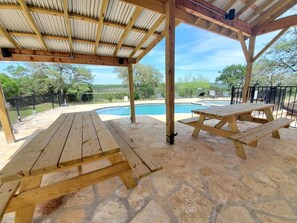 Uma área externa coberta com piscina, mesas de piquenique e piso de pedra.