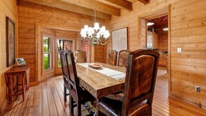 Une salle à manger en bois, agrémentée d’un lustre, avec des murs en bois et une vue sur l’extérieur.