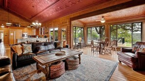 Un salon spacieux avec un plafond en bois, un grand canapé, une table basse et un coin repas comprenant des chaises et une table.