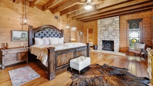 Une chambre spacieuse avec un grand lit, des poutres apparentes en bois au plafond, une cheminée en pierre et un décor de style rustique.