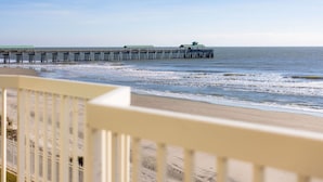 A beach with a wooden pier extending into the ocean, featuring several structures with green roofs.