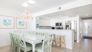A modern kitchen with white cabinets, stainless steel appliances, and a dining area with a glass table and green chairs.