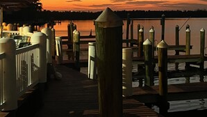 Une jetée en bois, dotée de garde-corps et de bornes, qui mène à une étendue d'eau calme au coucher du soleil.