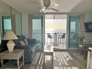 A living room with a sofa, a coffee table, a lamp, and a TV. There is a balcony with a table and chairs, and a view of the ocean. - MILLION DOLLAR UPDATED BEACHFRONT VIEW with a ROOM. Penthouse Floor Happy Guests (Marco Island)