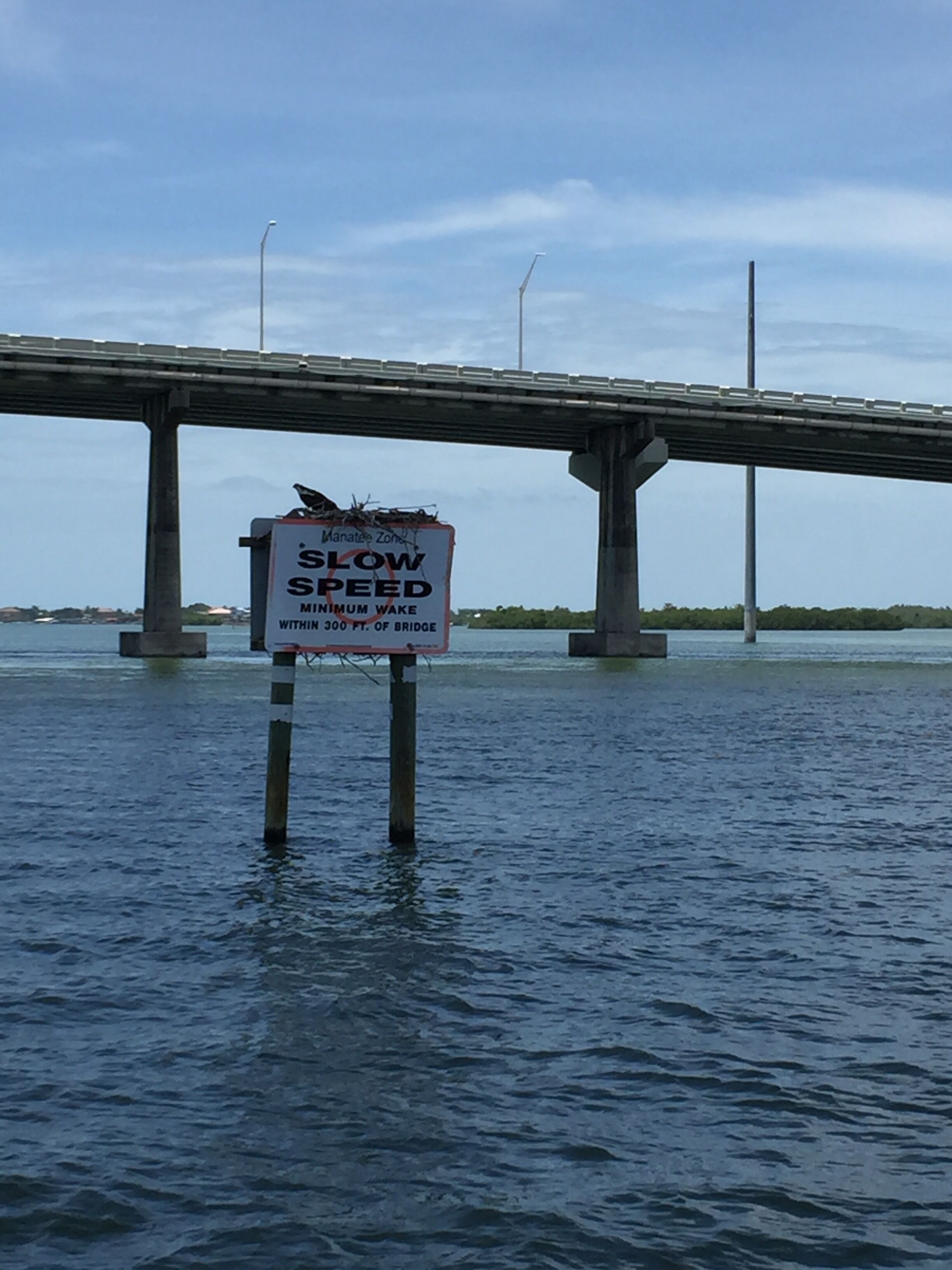 A bridge over water with a sign indicating a manatee zone and a minimum wake speed of 3 knots within 300 feet of the bridge.