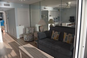 A living room with a grey sofa, a patterned armchair, a small table, and a lamp. There is a kitchen area visible through a glass partition. - MILLION DOLLAR UPDATED BEACHFRONT VIEW with a ROOM. Penthouse Floor Happy Guests (Marco Island)