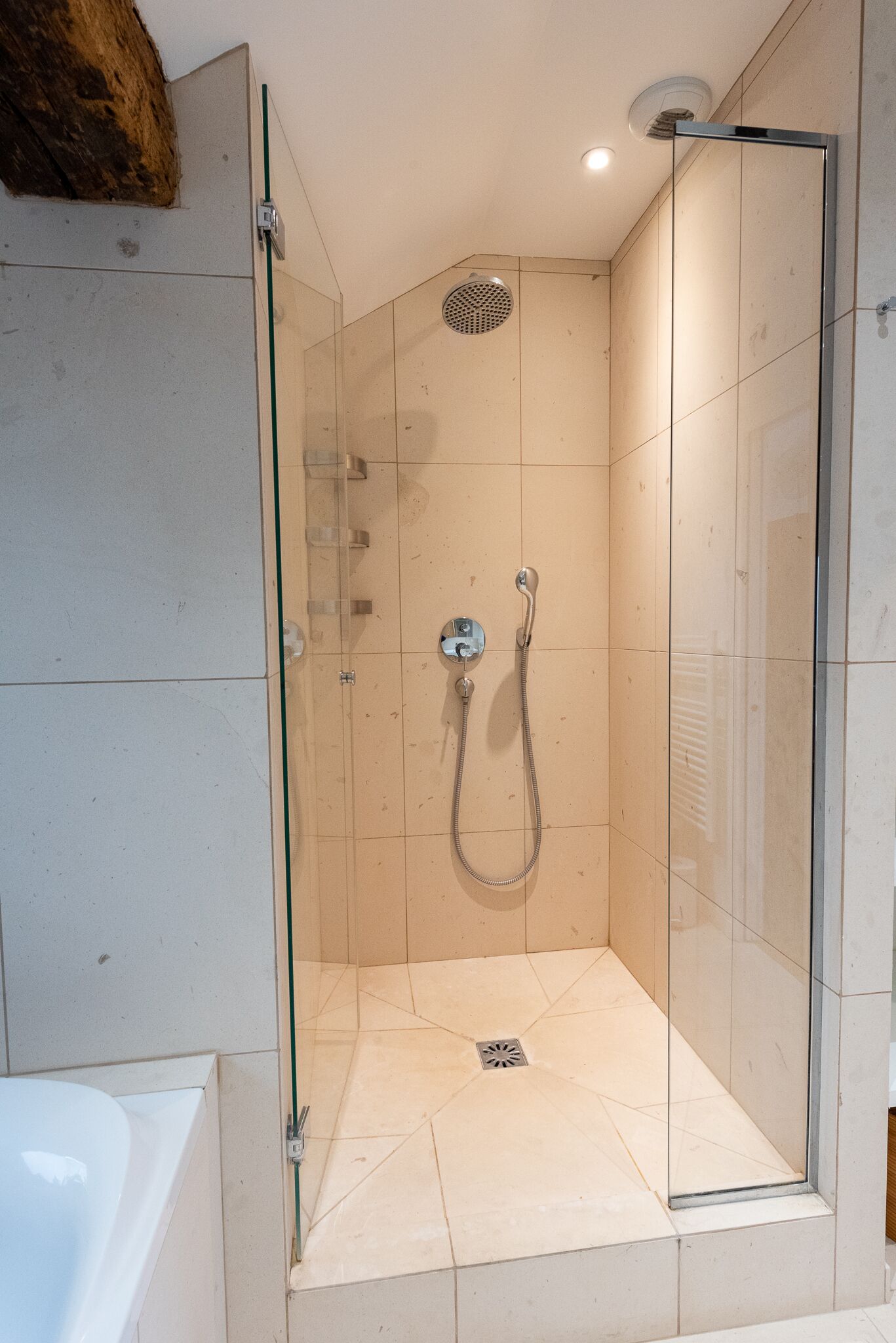 A glass-enclosed shower with a handheld showerhead and a wall-mounted control.