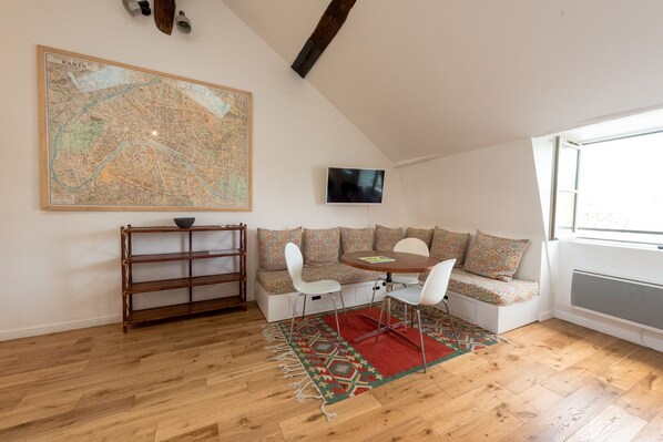 A cozy loft bedroom with a large map, a TV, a wooden floor, a patterned rug, and a built-in seating area.