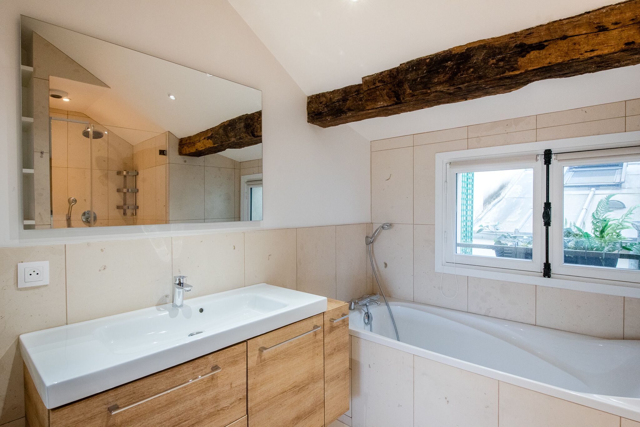 Un baño moderno con un espejo grande, un tocador de madera, una bañera y una ventana con vistas al exterior.