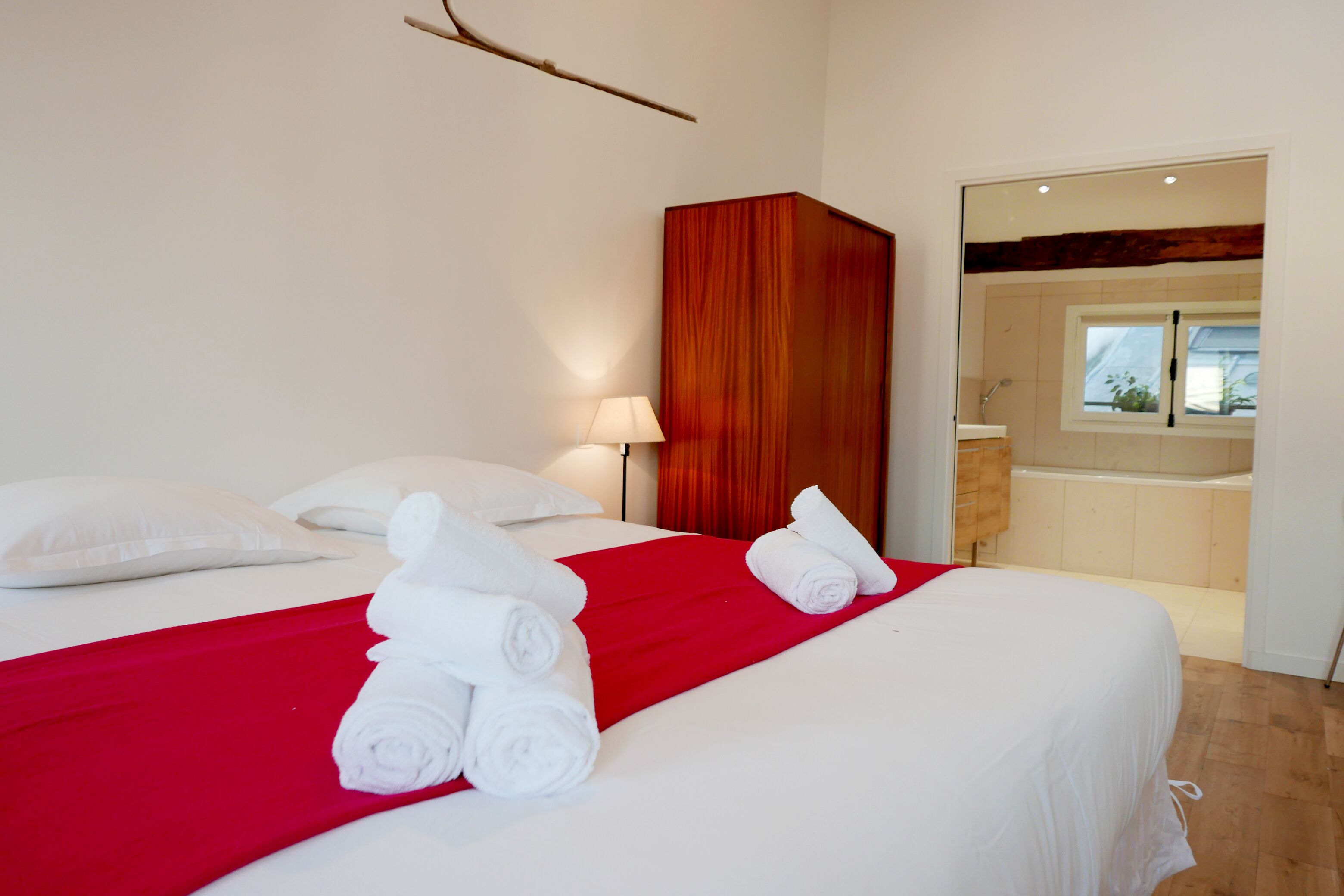 A hotel room with a bed, a red throw blanket, and neatly folded towels.