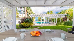 Un espacio para comer al aire libre con una mesa lista para dos, una piscina y vista al océano.