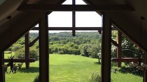 A room with a large window offering a view of a green field and forested hills. - Chalet on 250 acres, Private, 1 Mi from Chautauqua Institution / Lake (Mayville)