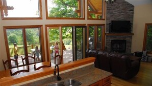 A modern kitchen with granite countertops, a double sink, and wooden cabinets. There is a stone fireplace and a television mounted above it. - Chalet on 250 acres, Private, 1 Mi from Chautauqua Institution / Lake (Mayville)
