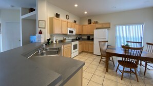 A modern kitchen with wooden cabinets, a stainless steel sink, a microwave, and a refrigerator. There is a dining table with chairs and a window with blinds. - Gorgeous Pool Home, Big Yard, 6 miles to Disney, Gated Resort, Amenities for All (Clermont)