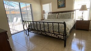 A bedroom with a bed, a ceiling fan, a painting, and a window with blinds. - Gorgeous Pool Home, Big Yard, 6 miles to Disney, Gated Resort, Amenities for All (Clermont)