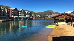 A waterfront hotel with paddleboarders on the water, a sandy beach, and mountain views in the background. - Mountain-chic retreat - sleeps 10  - room for everyone (Keystone)