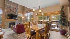 A spacious living room with a stone fireplace, a large wooden dining table, and a cozy red sofa. - Mountain-chic retreat - sleeps 10  - room for everyone (Keystone)