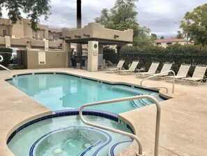 A swimming pool with a hot tub, surrounded by lounge chairs and a fence.