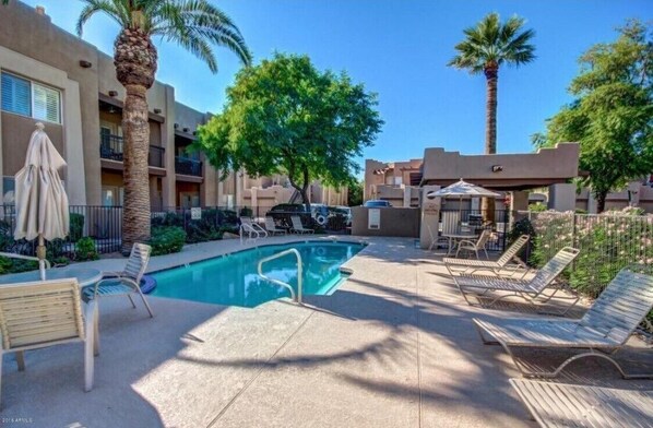 A pool area with lounge chairs, a palm tree, and a building with balconies.