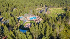 An aerial view of a resort with multiple swimming pools, a golf course, and dense forest surroundings.