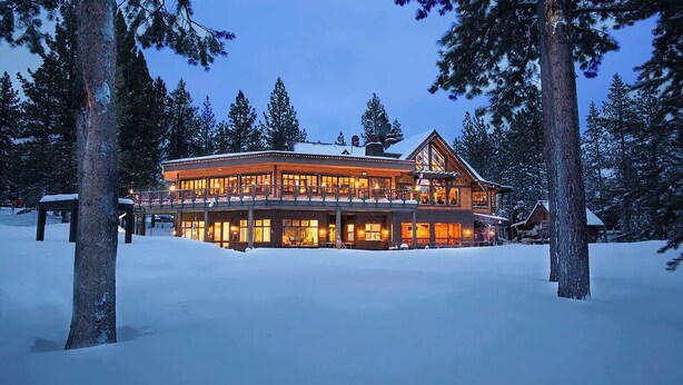 A large, multi-story lodge with a prominent central entrance, surrounded by snow-covered ground and tall pine trees.