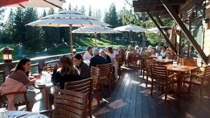An outdoor dining area with wooden tables and chairs, umbrellas, and a view of a golf course.